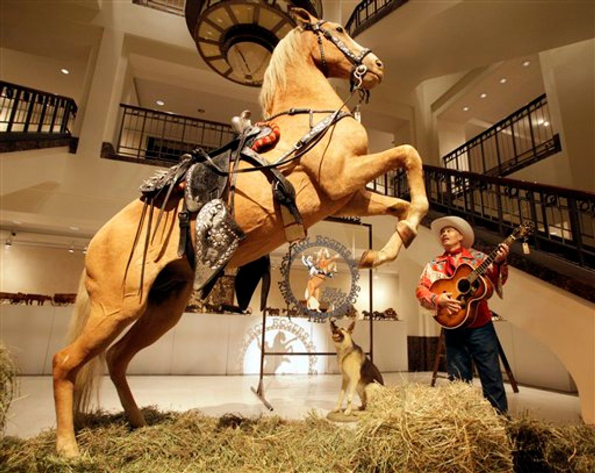 Gil Perez, right, a doorman at Christies auction house, wears an outfit and holds a guitar belonging  to Roy Rogers as he stands alongside the preserved remains of Rogers' horse "Trigger" and dog "Bullet"  at  the New York auction house,  Friday, July 9, 2010.  Christie's held a preview Friday of an upcoming auction of items from the now-closed Roy Rogers and Dale Evans Museum in Branson, Mo. (AP Photo/Richard Drew) (AP)