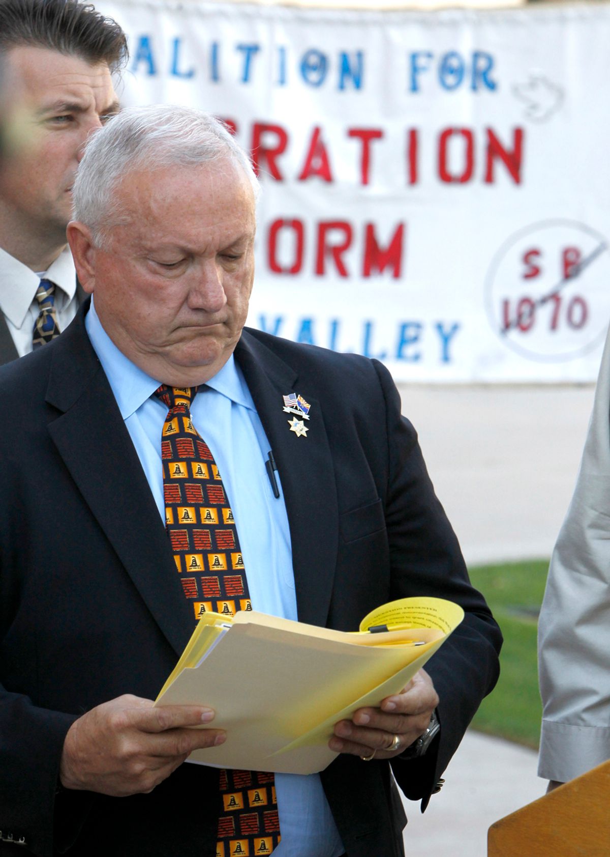 With protesters holding a sign in the background, Arizona state Sen. Russell Pearce, R-Mesa, checks notes before speaking at a news conference about efforts by state legislators to propose legislation to deny U.S. citizenship to children of illegal immigrants Tuesday, Oct. 19, 2010, in Phoenix.  The efforts by the state legislators come amid calls to change the U.S. Constitution's 14th Amendment, which grants automatic citizenship to U.S.-born children of illegal immigrants. (AP Photo/Ross D. Franklin)  (Ross D. Franklin)