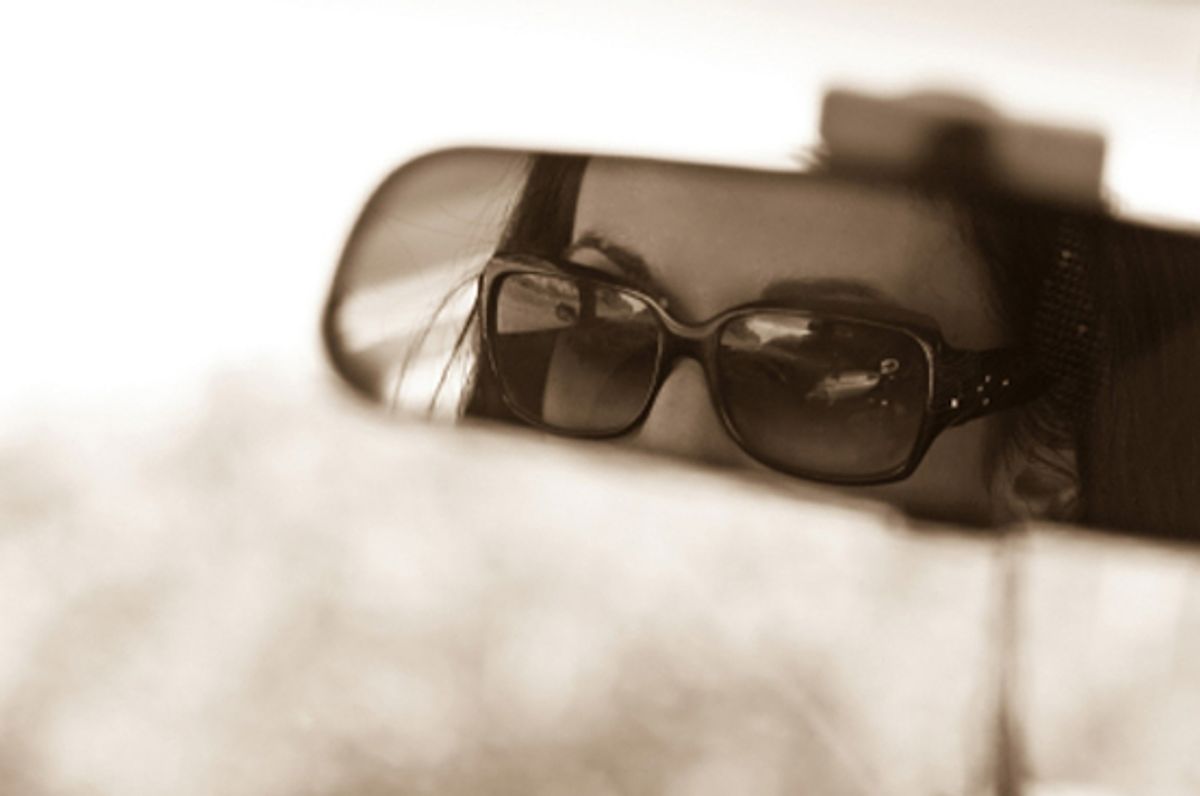 The face of a young woman driving as seen in the rear view mirror. (Unknown)