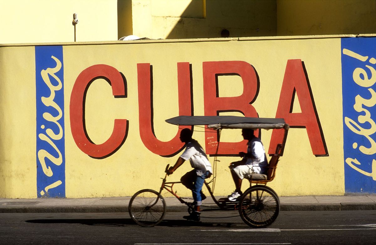 A2REAC Cuba Havana bicycle taxi moving past Viva Cuba wall mural (Alamy)