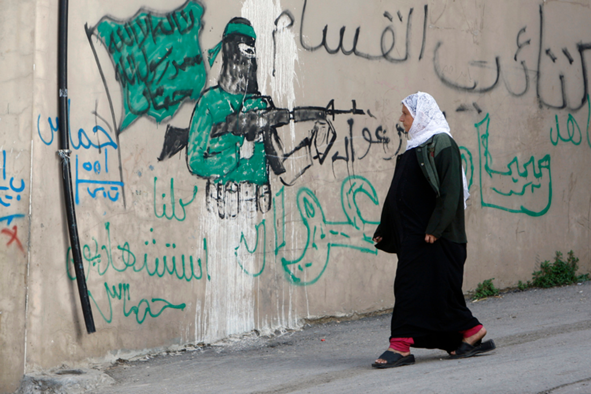 A Palestinian woman walks past a wall with graffiti depicting a gunman