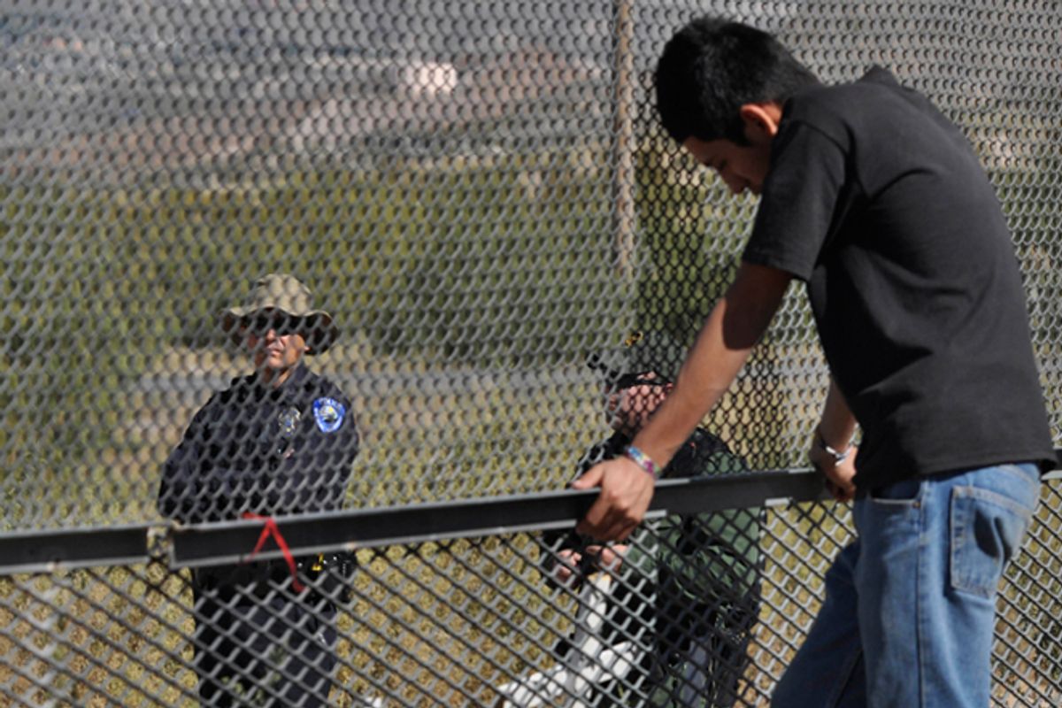 A man in Ciudad Juarez, Mexico, stands next to the border fence as two U.S. law enforcement officers look on from the U.S. side of the fence.        (AP/Raymundo Ruiz)