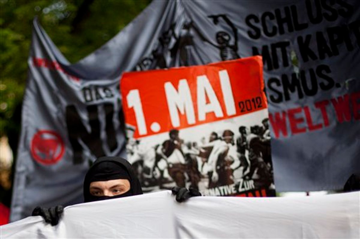 A masked left-wing protester holds a poster as he walks with other demonstrators at a rally to mark May Day in Berlin's district Kreuzberg, Tuesday, May 1, 2012.        (AP Photo/Markus Schreiber)