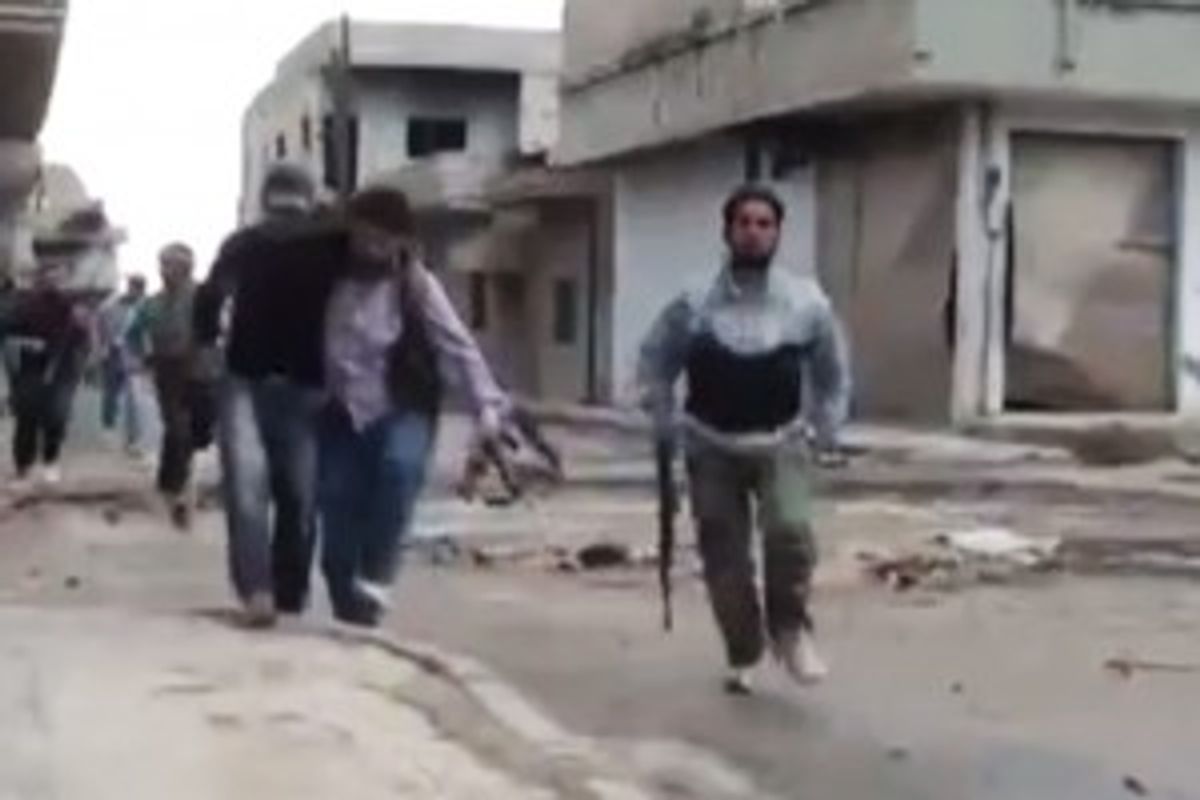 This image, made from amateur video released by the Shaam News Network and accessed Monday, May 14, 2012, purports to show a Syrian rebel helping an injured man in Rastan, Homs, Syria.              (AP Photo/Shaam News Network via AP video)