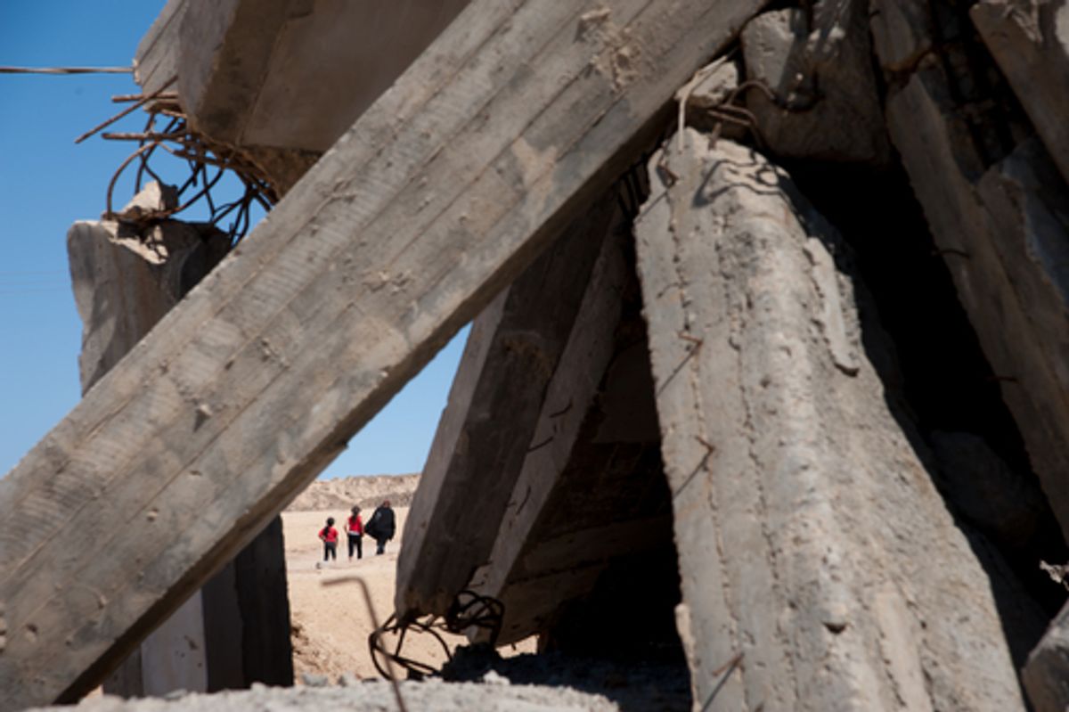  Palestinians in Gaza walk by damage from an Israeli shelling (Shutterstock)    