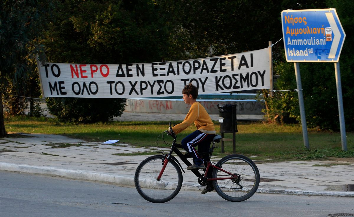 A boy cycles past a banner which reads in Greek "All the gold in the world can't buy water" at the village of Ierissos in the Halkidiki peninsula in northern Greece.    (AP/Nikolas Giakoumidis)