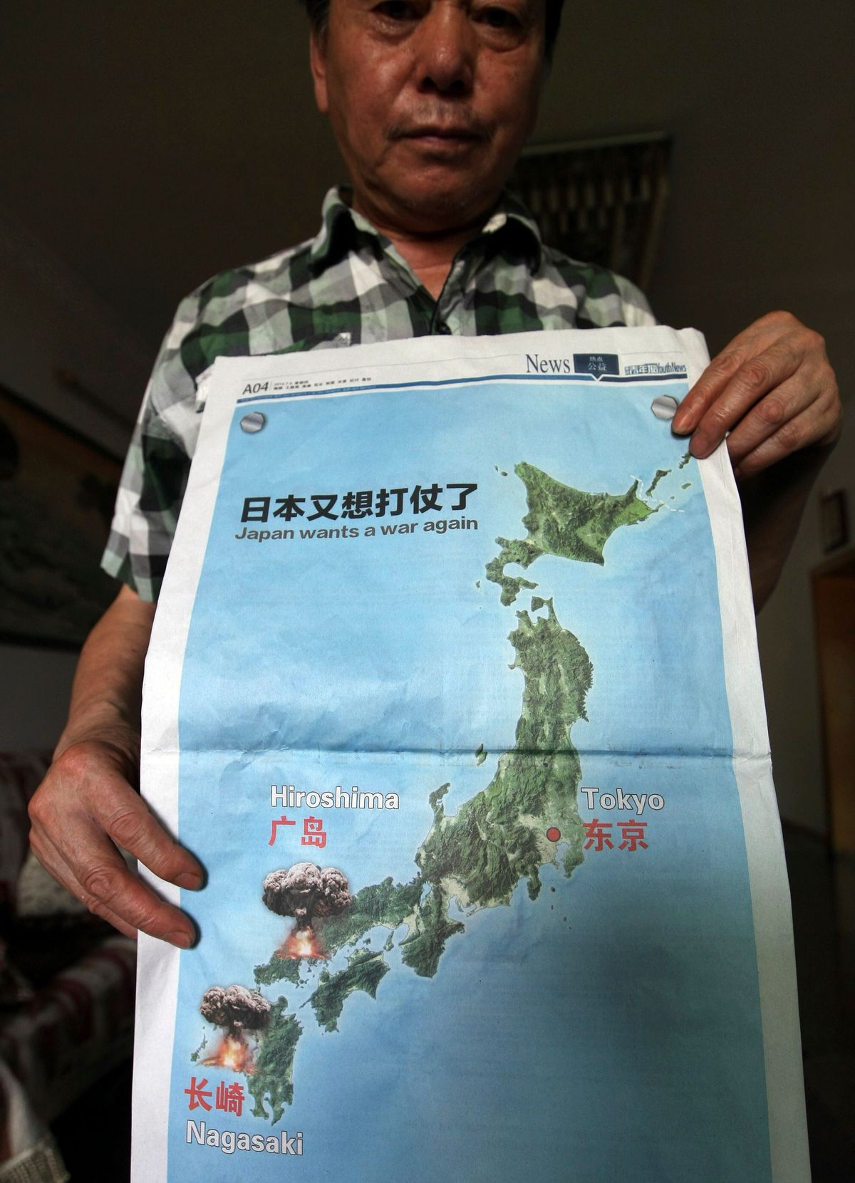 A man poses with a full page map with the headline "Japan wants a war again" and showing mushroom clouds over Hiroshima and Nagasaki that was published on the July 3, 2014 issue of the Chongqing Youth Daily newspaper, days after Japan reinterpreted its war-renouncing constitution to allow a greater military role,  in Chongqing, China, Wednesday, July 9, 2014.  Japan has protested to China over cartoon drawings of exploding mushroom clouds in a Japanese map published in the newspaper last week, saying the graphic offended the atomic bombing survivors and their relatives. (AP Photo) CHINA OUT (AP)