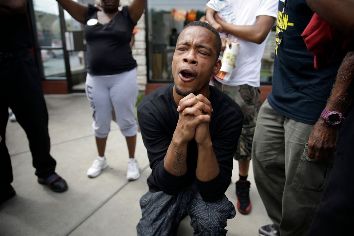 A man bends down in prayer as police try to disperse a small group of protesters Monday, Aug. 18, 2014, in Ferguson, Mo. The Aug. 9 shooting of Michael Brown by police has touched off rancorous protests in Ferguson, a St. Louis suburb where police have used riot gear and tear gas. Gov. Jay Nixon ordered the National Guard to help restore order Monday, while lifting a midnight-to-5 a.m. curfew that had been in place for two days. (AP Photo/Jeff Roberson) (AP)