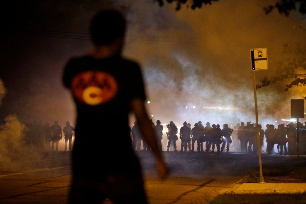 FILE - In this Aug. 13, 2014 file photo, a man watches as police walk through a cloud of smoke during a clash with protesters in Ferguson, Mo. The response to Browns death turned violent because of a convergence of factors, observers said.  (AP/Jeff Roberson)