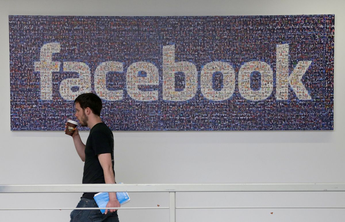 FILE - In this March 15, 2013, file photo, a Facebook employee walks past a sign at Facebook headquarters in Menlo Park, Calif.   (AP/Jeff Chiu)