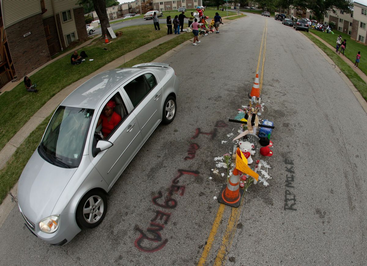 In this Aug. 15, 2014, file photo, a car drives past a memorial in the middle of the street where Michael Brown was shot by police in Ferguson, Mo. Six months after 18-year-old Michael Brown died in the street in Ferguson, Missouri, the Justice Department is close to announcing its findings in the racially charged police shooting that launched "hands up, don't shoot" protests across the nation. (AP Photo/Charlie Riedel)