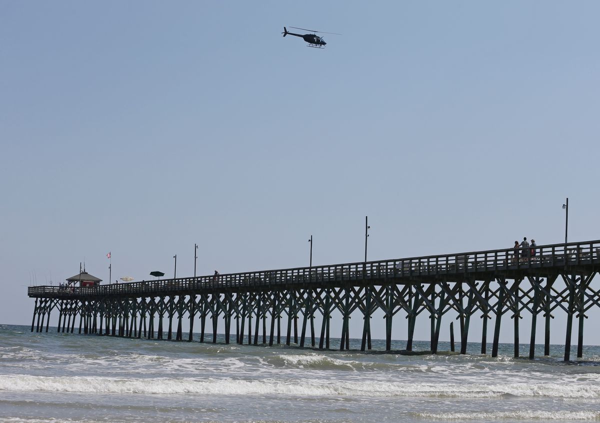 A helicopter flies over the Ocean Crest Pier in Oak Island, N.C., Monday, June 15, 2015. A 12-year-old girl from Asheboro lost part of her arm and suffered a leg injury, and a 16-year-old boy from Colorado lost his left arm about an hour later and 2 miles away in two separate shark attacks late Sunday afternoon.  (AP/Chuck Burton)