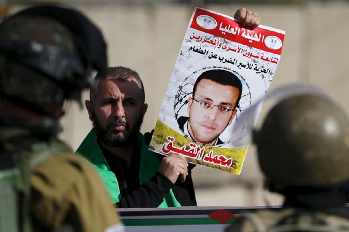 A Palestinian protester standing in front of Israeli soldiers holds the picture of imprisoned journalist Mohammad al-Qiq, near the occupied West Bank city of Ramallah on Jan. 22, 2016.   (Reuters/Mohamad Torokman)