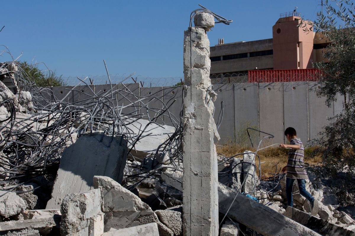 A Palestinian boy walks over the rubble of a house that overlooks the Israeli separation barrier, background, and was demolished by the Israeli army, in the West Bank village of Qalandia, near Ramallah, Tuesday, July 26, 2016.  (AP)