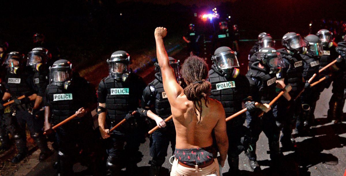 A protester stands with his left arm extended and fist clenched in front of a line of police officers in Charlotte, N.C. on Tuesday, Sept. 20, 2016. Authorities used tear gas to disperse protesters in an overnight demonstration that broke out Tuesday after Keith Lamont Scott was fatally shot by an officer at an apartment complex. (Jeff Siner/The Charlotte Observer via AP) (AP)