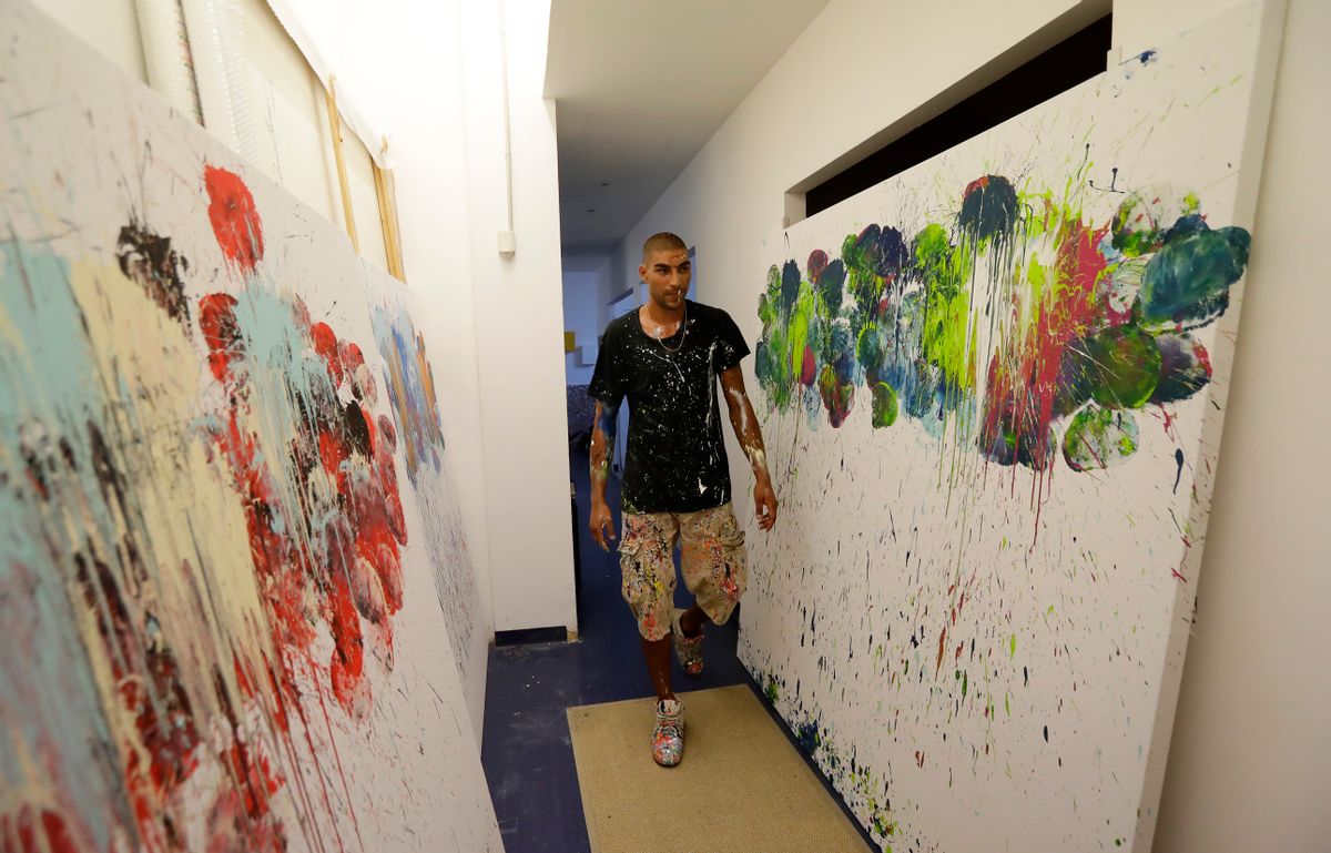 In this photo taken on Tuesday, Sept. 6, 2016 Omar Hassan walks past his creations "Breaking Through" in his studio in Milan, Italy. When he creates art work, Omar Hassan doesn’t get out paint brushes. He gets out his boxing gloves. Hassan, a 29-year-old artist and boxer, has combined his two passions, with the goal to bring the disciplines closer. Hassan, born in Milan to an Italian mother and Egyptian father, creates the works by dipping his glove in paint, and punching the canvas stretched over cardboard to keep it from breaking. He calls the series ‘’Breaking Through Milano’’ His paintings sell from 8,000 to 40,000 euros, which he calls ‘’a great satisfaction, but not the goal.’’ (AP Photo/Antonio Calanni) (AP)