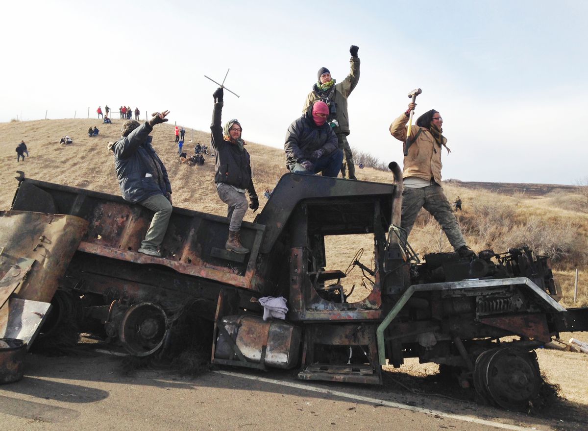 FILE - In this Monday, Nov. 21, 2016, file photo, protesters against the Dakota Access oil pipeline stand on a burned-out truck near Cannon Ball, N.D., that they removed from a long-closed bridge a day earlier on a state highway near their camp in southern North Dakota. President-elect Donald Trump holds stock in the company building the disputed Dakota Access oil pipeline, and pipeline opponents warn that Trump’s investments could undercut any decision he makes on the $3.8 billion project as president. (AP Photo/James MacPherson, File) (AP)