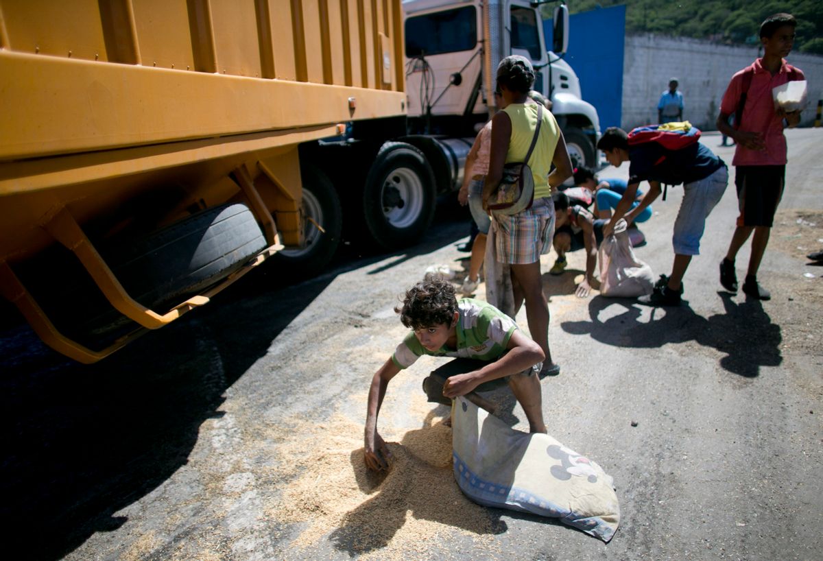 FILE - In this Nov. 14, 2016 file photo, a youth uses his pillow as a bag to collect rice from the pavement that shook loose from a food cargo truck waiting to enter the port in Puerto Cabello, Venezuela, the port that handles the majority of Venezuela's food imports. The calls by members of Congress on both sides of the aisle to sanction Venezuelan officials for profiting from food shortages come in response to an Associated Press investigation that found trafficking in hard-to-find food has become big business in Venezuela, with the military at the heart of the graft. (AP Photo/Ariana Cubillos, File) (AP)