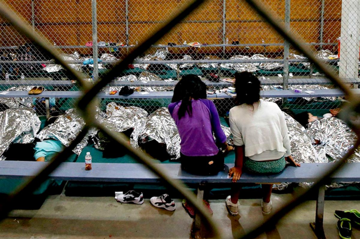 Two young girls watch television from their holding area where hundreds of mostly Central American immigrant children are being processed and held at the U.S. Customs and Border Protection Nogales Placement Center   (AP/Ross D. Franklin)