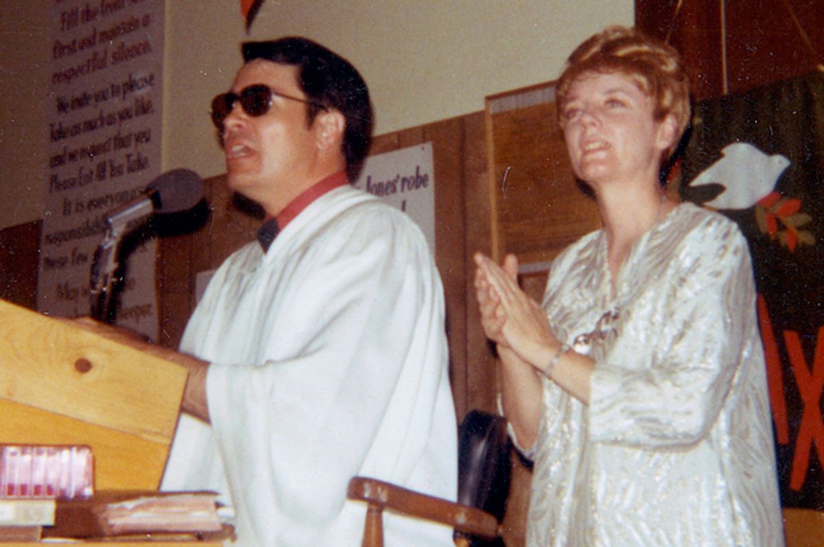 Jim Jones leading a Peoples Temple service, with Marceline standing behind him. Jones kept a vessel on a shelf behind his podium so he could discreetly relieve himself during hours-long Temple services. (Special Collections and University Archives, San Diego State University Library & Information Access)