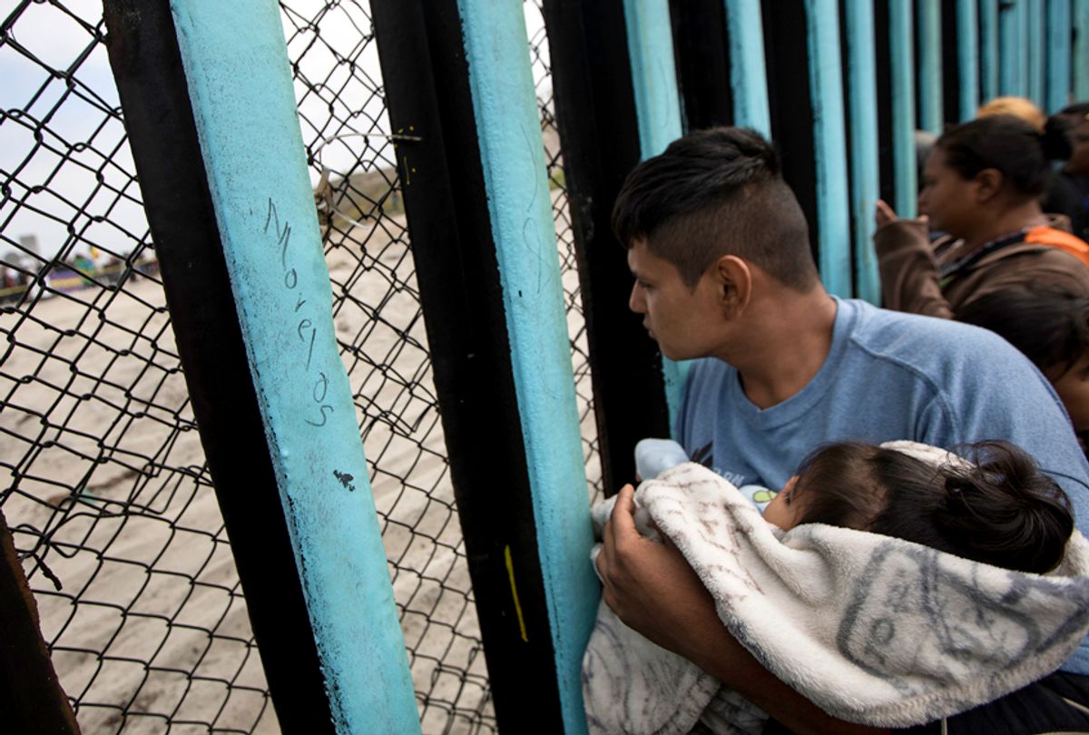 A member of the Central American migrant caravan, holding a child, looks through the U.S./Mexico border wall. (AP/Hans-Maximo Musielik)