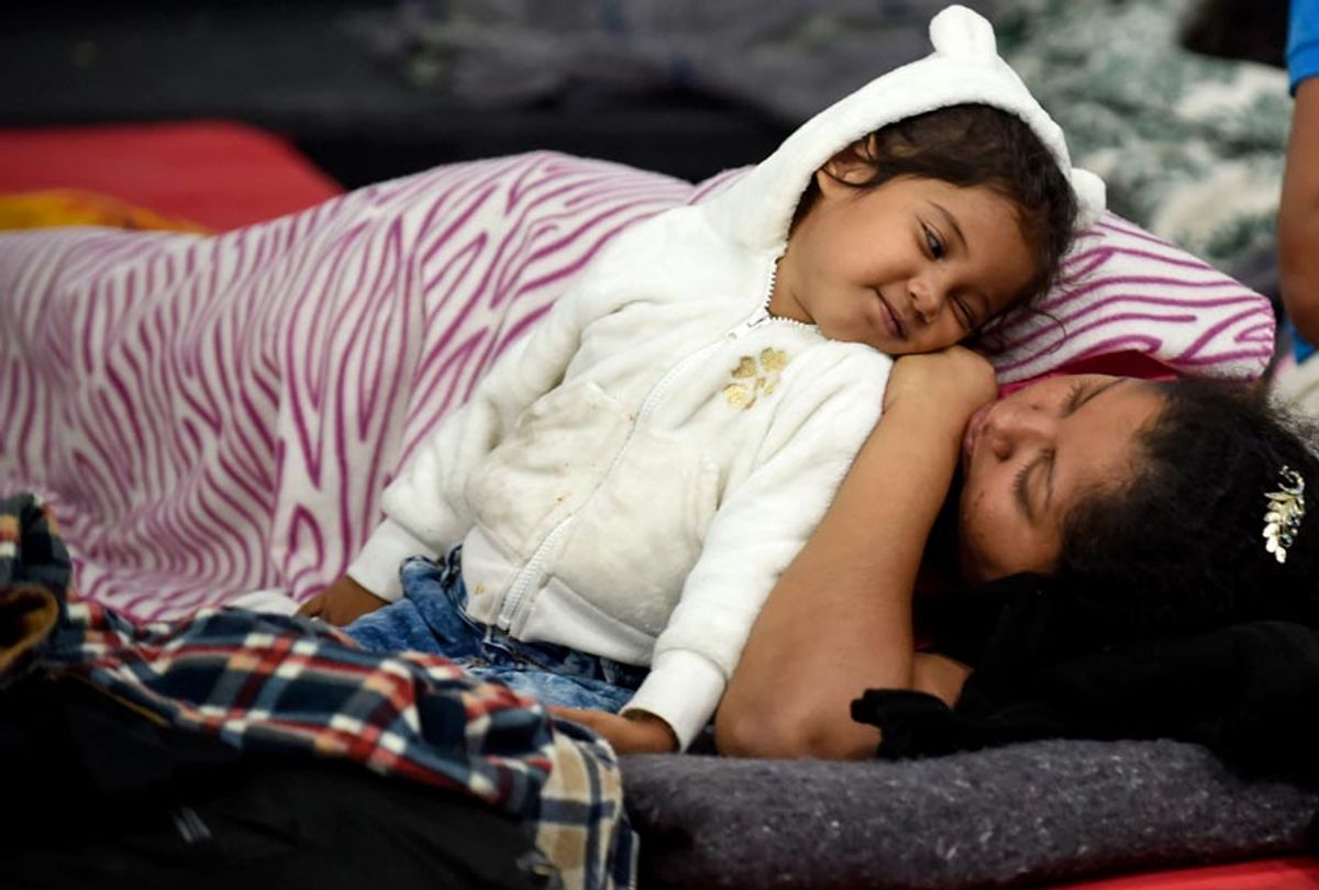 A migrant woman and her daughter, who are taking part in a caravan towards the US, cuddle up to rest during a stop in their journey in Mexico City, on November 6, 2018. (Getty/Alfredo Estrella)