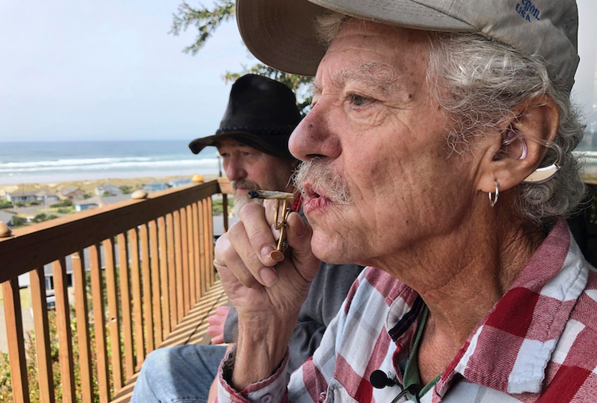 In this photo taken April 25, 2019, two-time cancer survivor and medical marijuana cardholder Bill Blazina, 73, smokes a marijuana joint on the deck of his neighbor’s home in Waldport, Ore. (AP Photo/Gillian Flaccus)