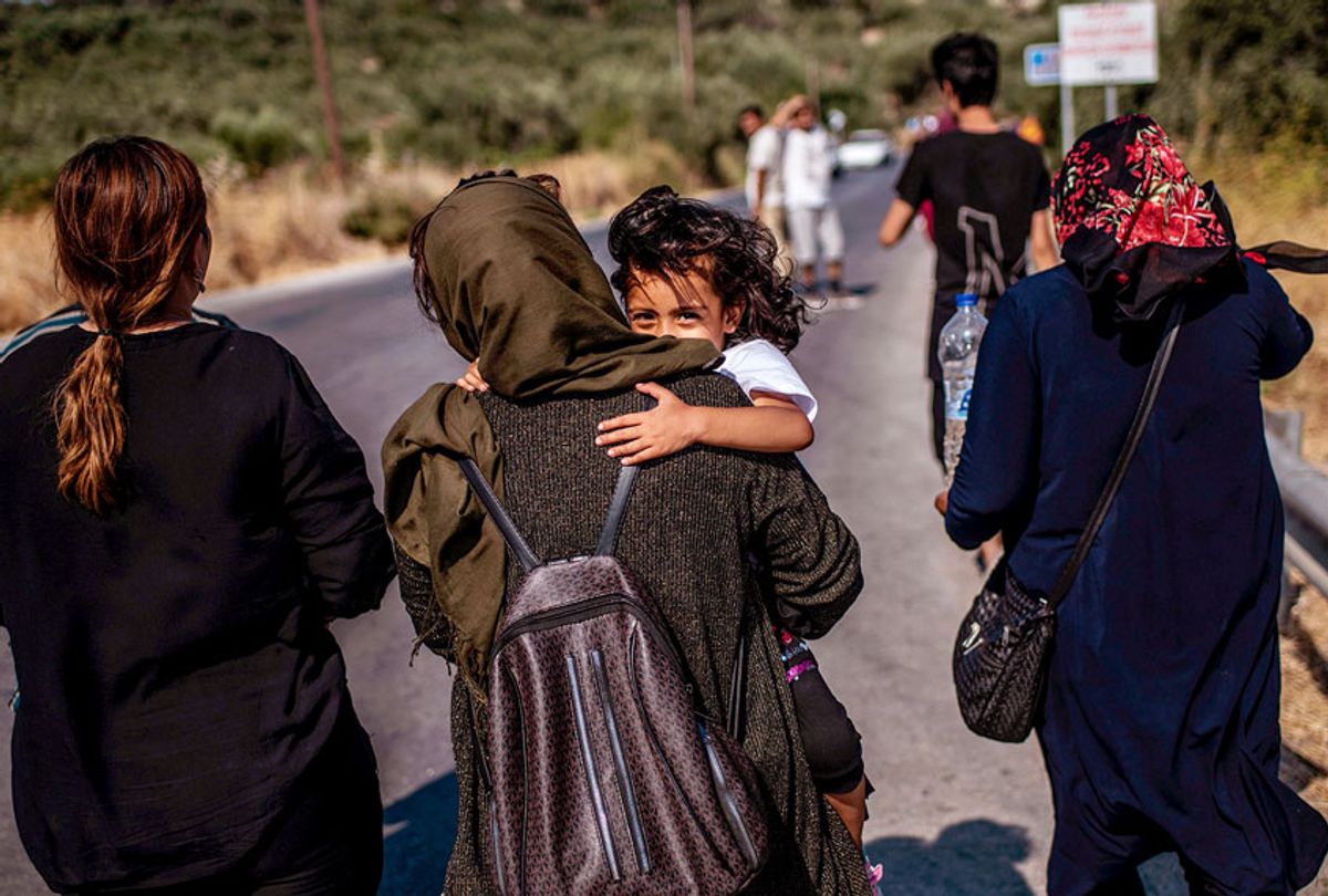 A migrant woman carries a little girl as they walk in a street. (Getty/Angelos Tzortzinis)