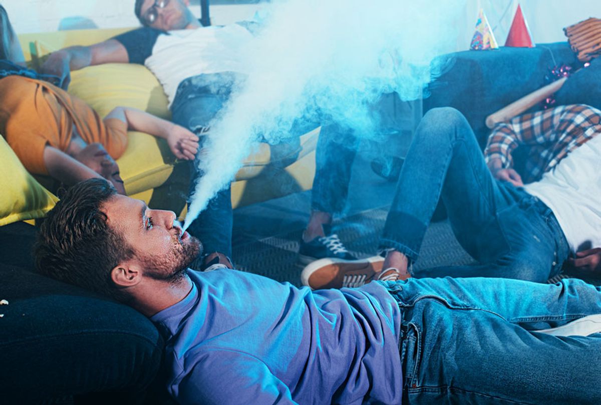 Young man smoking electronic cigarette while drunk friends sleeping after party (Getty Images/ LightFieldStudios)