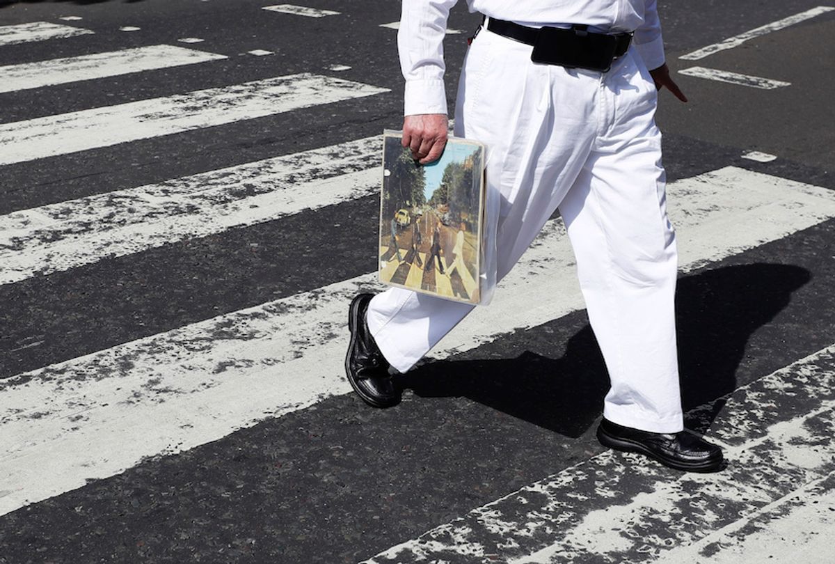 A fan carries a copy of the album 'Abbey Road' as he crosses the Abbey Road zebra crossing on the 50th anniversary of British pop musicians The Beatles doing it for their album cover of 'Abbey Road' in St Johns Wood in London, Thursday, Aug. 8, 2019. (AP Photo/Kirsty Wigglesworth)