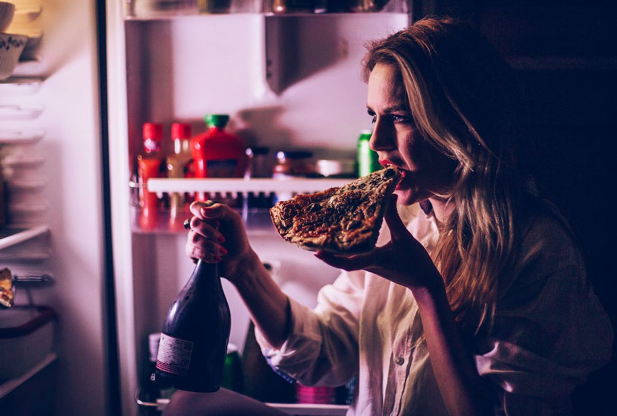 Woman eating pizza and drinking wine in front of the refrigerator during the night (Getty Images)