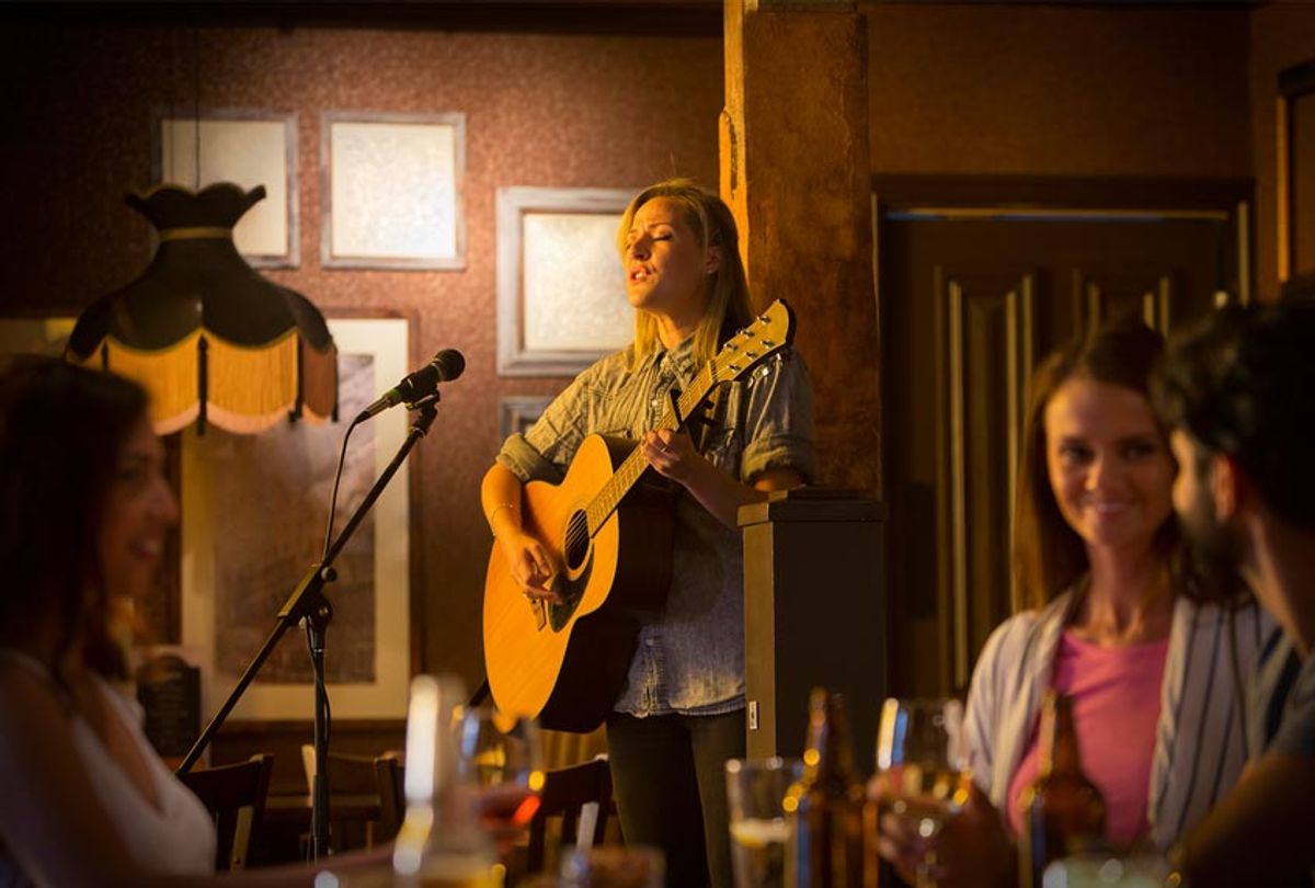 A young woman sings and plays her guitar in a pub. (Getty Images)