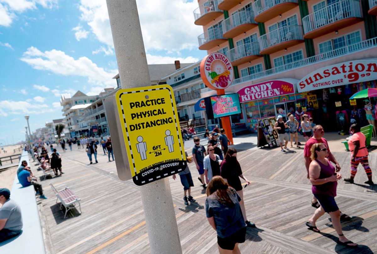 People walk past a sign advising about social distancing on the boardwalk during the Memorial Day holiday weekend amid the coronavirus pandemic on May 23, 2020 in Ocean City, Maryland. (ALEX EDELMAN/AFP via Getty Images)