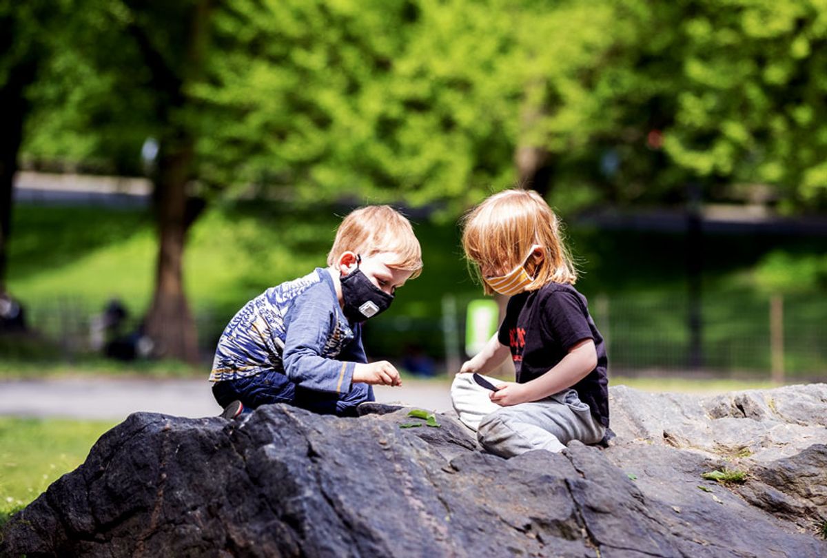 Two children wear a masks (personal protective equipment) while sitting on the rocks and playing with leaves in Central Park (Ira L. Black/Corbis via Getty Images)