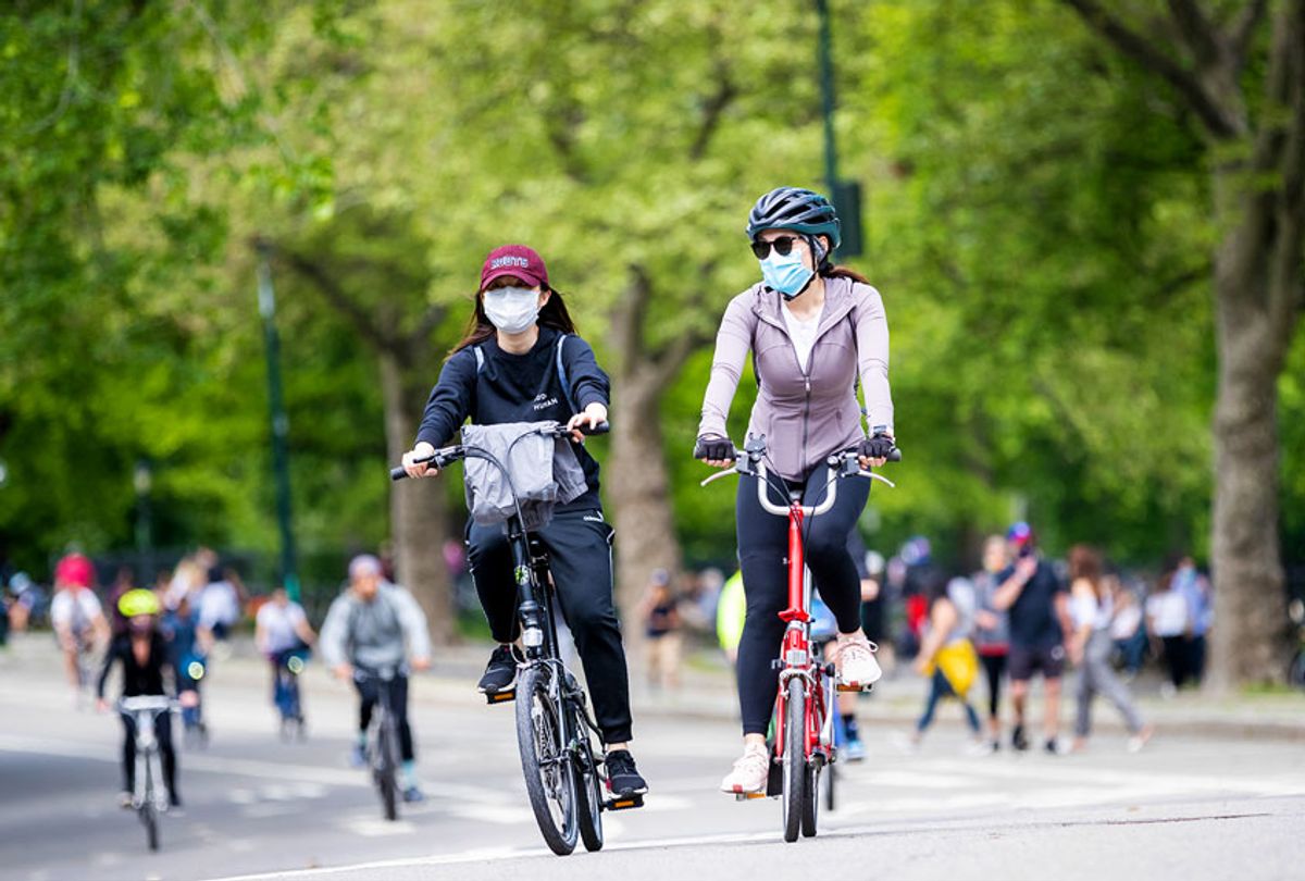 Two women wear masks (personal protective equipment) and ride bicycles in Central Park with other riders (Ira L. Black/Corbis via Getty Images)