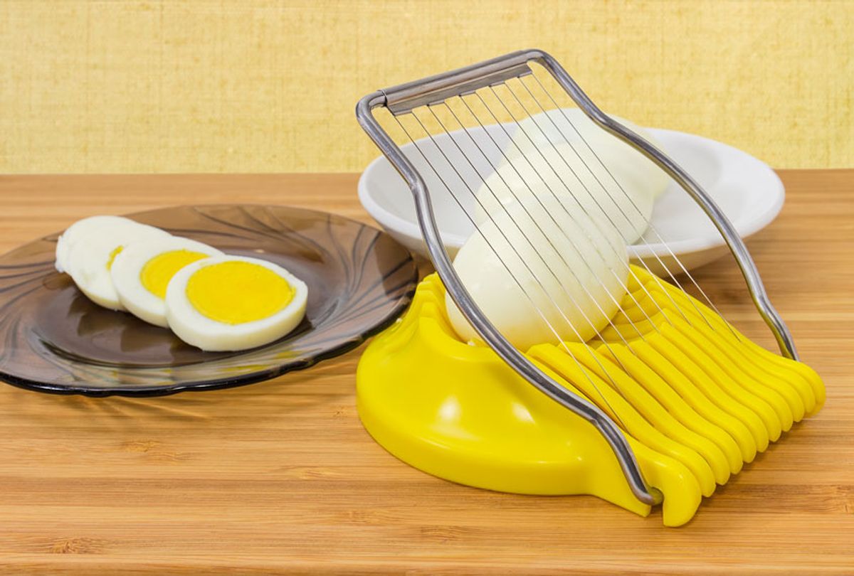Egg slicer with egg in it, sliced and whole peeled boiled eggs on a different saucers on a wooden bamboo surface at selective focus (Getty Images)