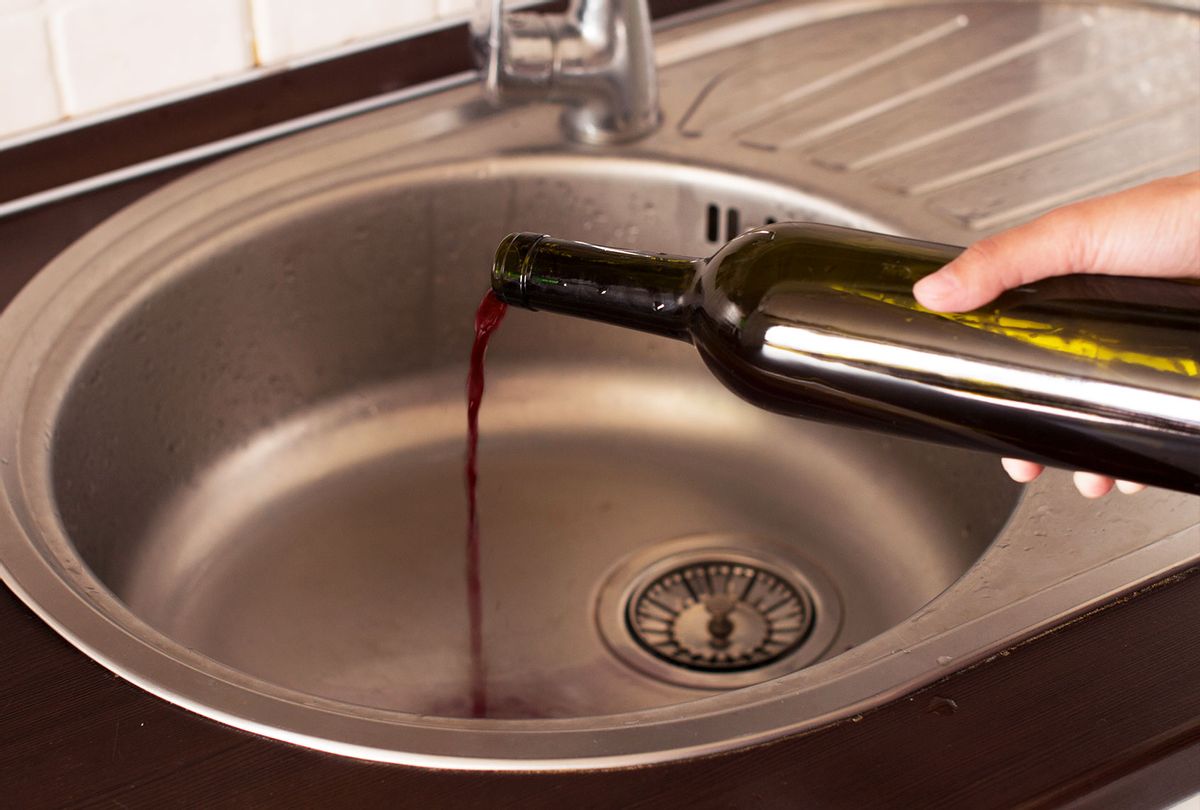 Young woman dumping wine from a bottle down the drain (Getty Images)