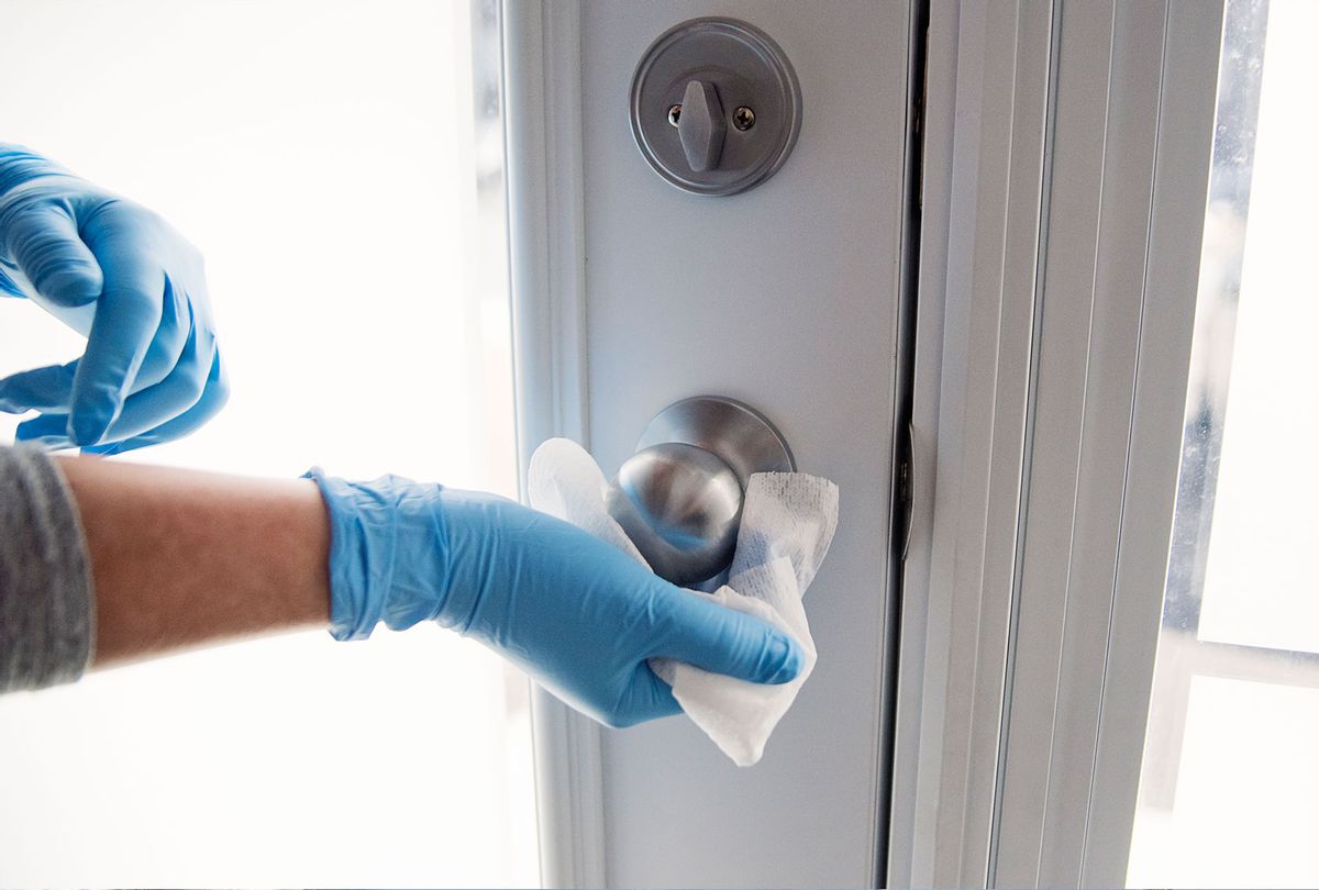 Hands with glove wiping doorknob (Getty Images)