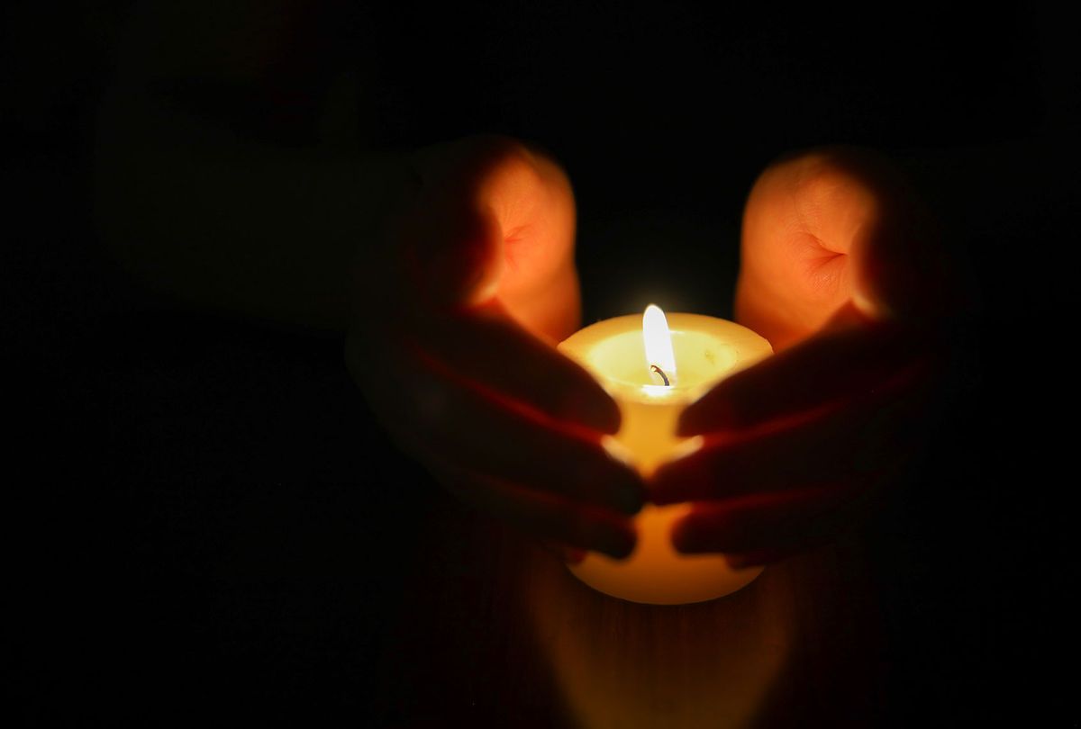 Hands protecting burning candle candlelight in darkness (Getty Images)