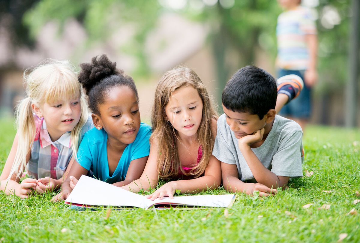 A Group of elementary-aged children is reading a book in the park. (Getty Images)