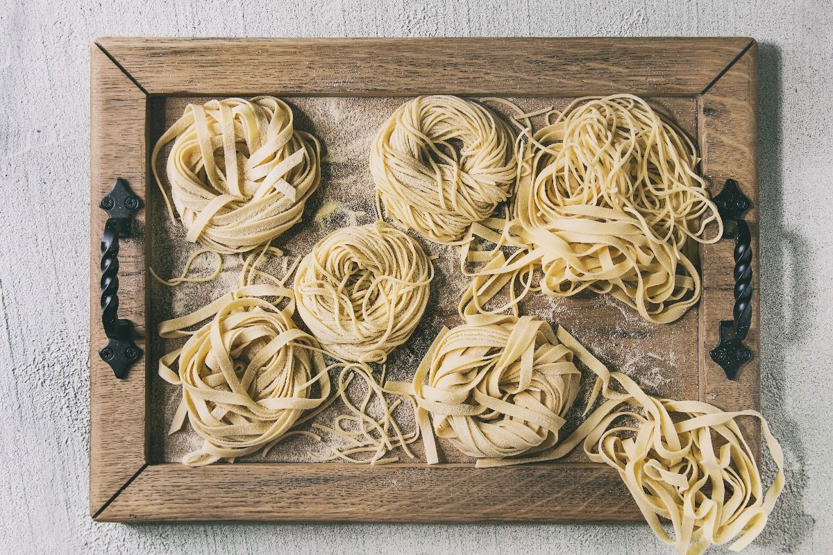 Variety of italian homemade raw uncooked pasta spaghetti and tagliatelle with semolina flour on wooden tray. (Getty Images)