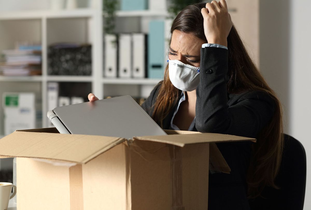 Fired executive woman with protective mask packing personal belongings on a box at the office at night (Getty Images)