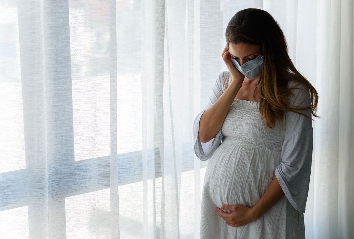 Pregnant woman standing by the big window with face medical mask on (Getty Images)