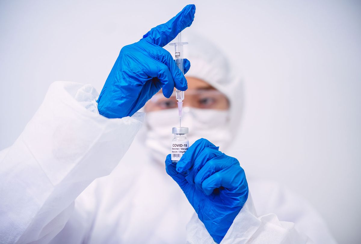 Doctor in protective gloves & workwear filling injection syringe with COVID-19 vaccine (Getty Images)