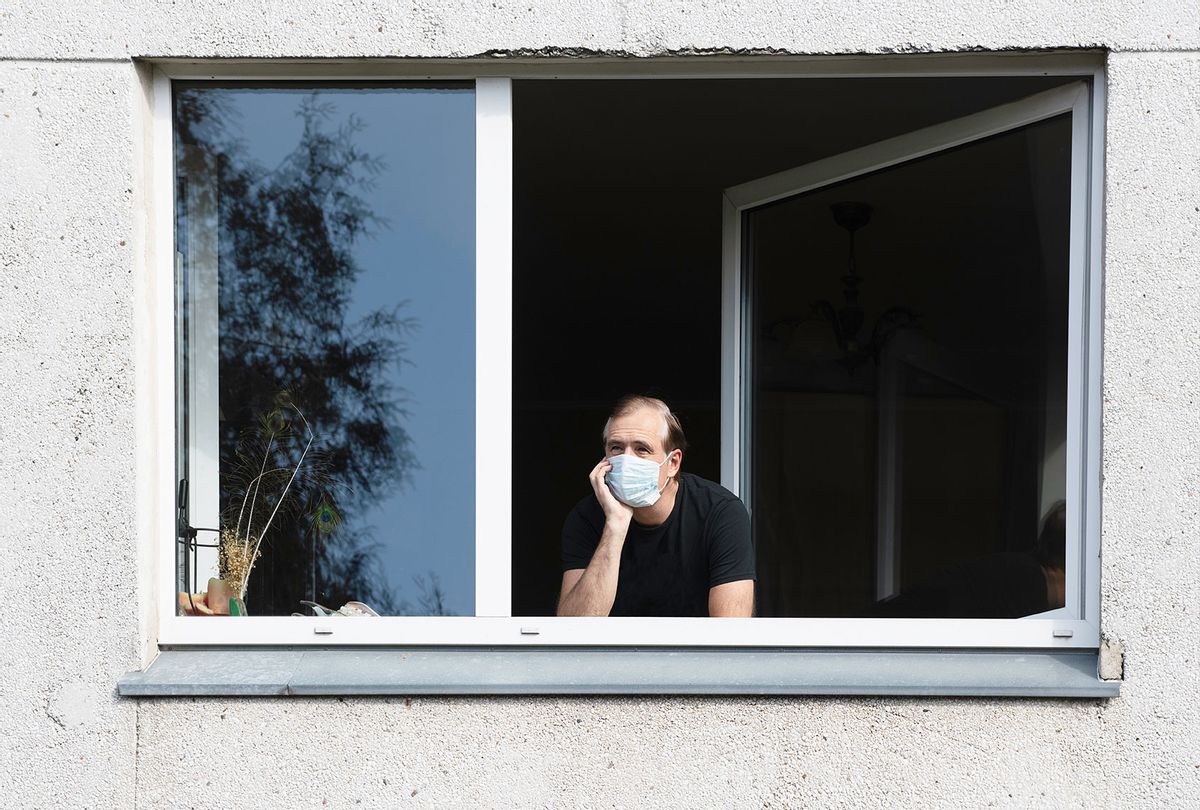 Man wearing a face mask looking out of a window (Getty Images)