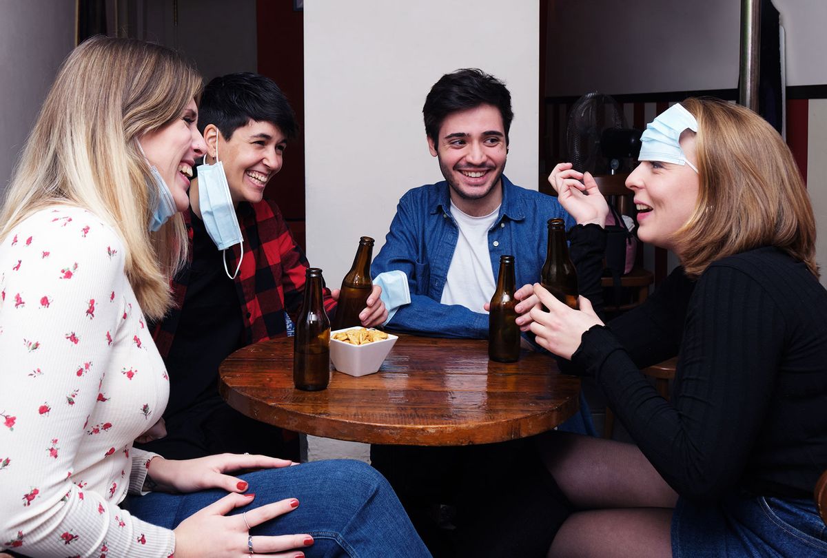 Four friends laughing around a table wearing their face protective masks incorrectly. (Getty Images)