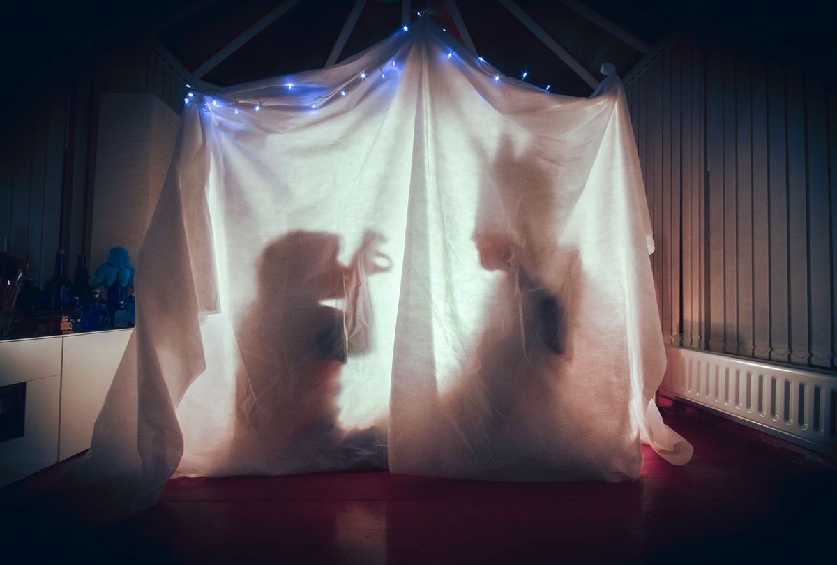 A parent and child tell each other stories inside a cosy tent lit up in a dark room of their home (Getty Images)