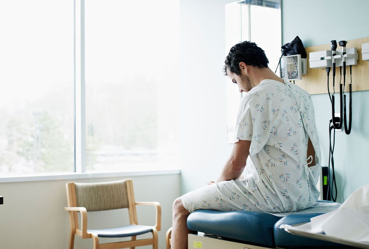 Male patient in gown waiting on exam table (Getty Images/Thomas Barwick)