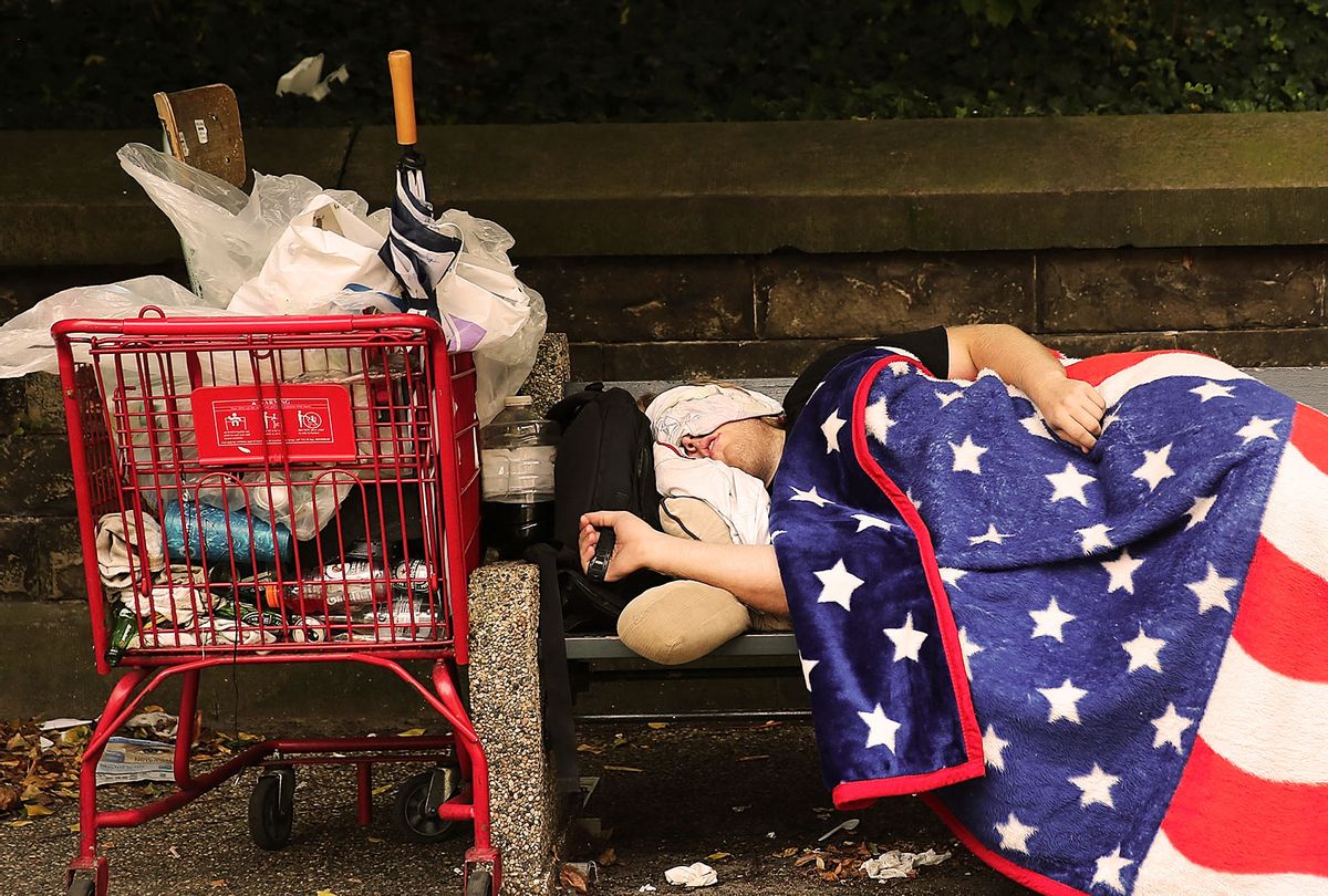 A homeless man sleeps under an American Flag blanket on a park bench. (Spencer Platt/Getty Images)