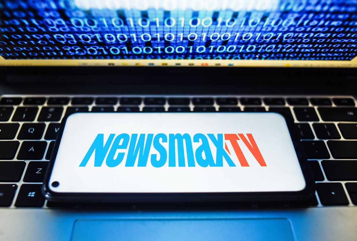 Newsmax TV logo seen displayed on a smartphone with binary code on a laptop screen. (Photo Illustration by Omar Marques/SOPA Images/LightRocket via Getty Images (Photo illustration by Salon/Omar Marques/SOPA Images/LightRocket/Getty Images/WikiCommons)
